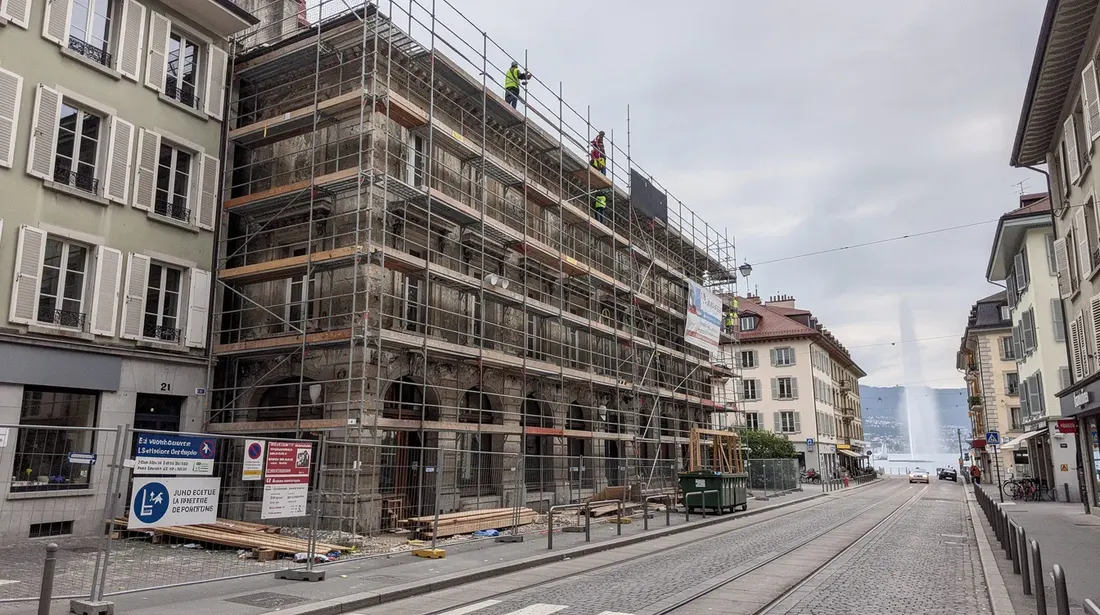 L'image montre un immeuble ancien en rénovation à Genève, entouré d'échafaudages qui témoignent des travaux en cours. Cette scène illustre le projet de rénovation d'un bâtiment, mettant en avant l'architecture et les efforts des bâtisseurs pour préserver le patrimoine tout en intégrant des éléments modernes.