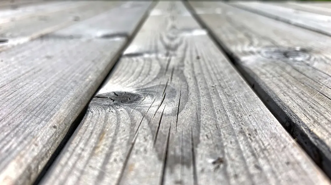 Gros plan sur des lames de terrasse en mélèze, présentant une patine grise argentée naturelle due à l'exposition extérieure au fil des années. Cette image met en avant la beauté et la durabilité des lames de terrasse en bois, idéales pour créer un espace de bien-être dans votre jardin.
